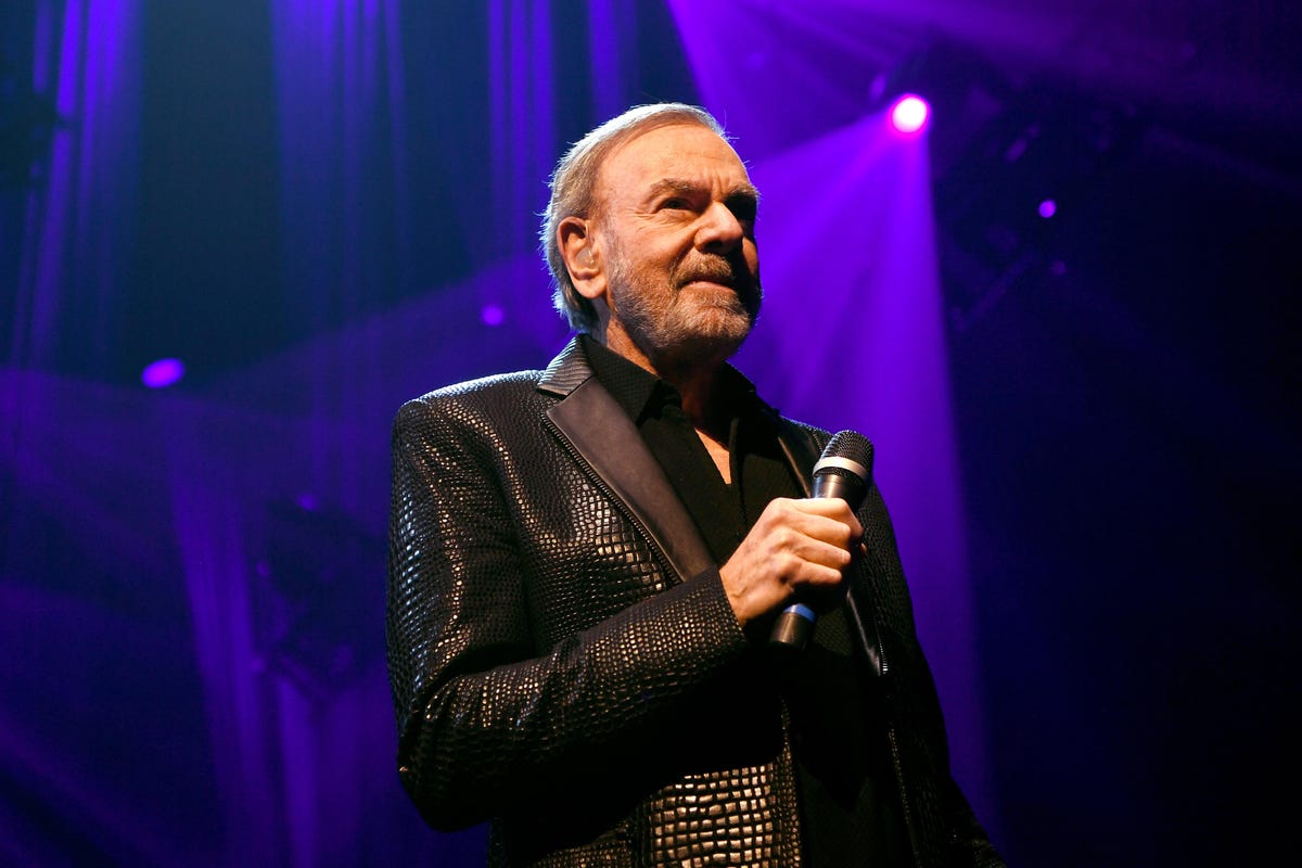 Neil Diamond wearing a black coat while holding a mic