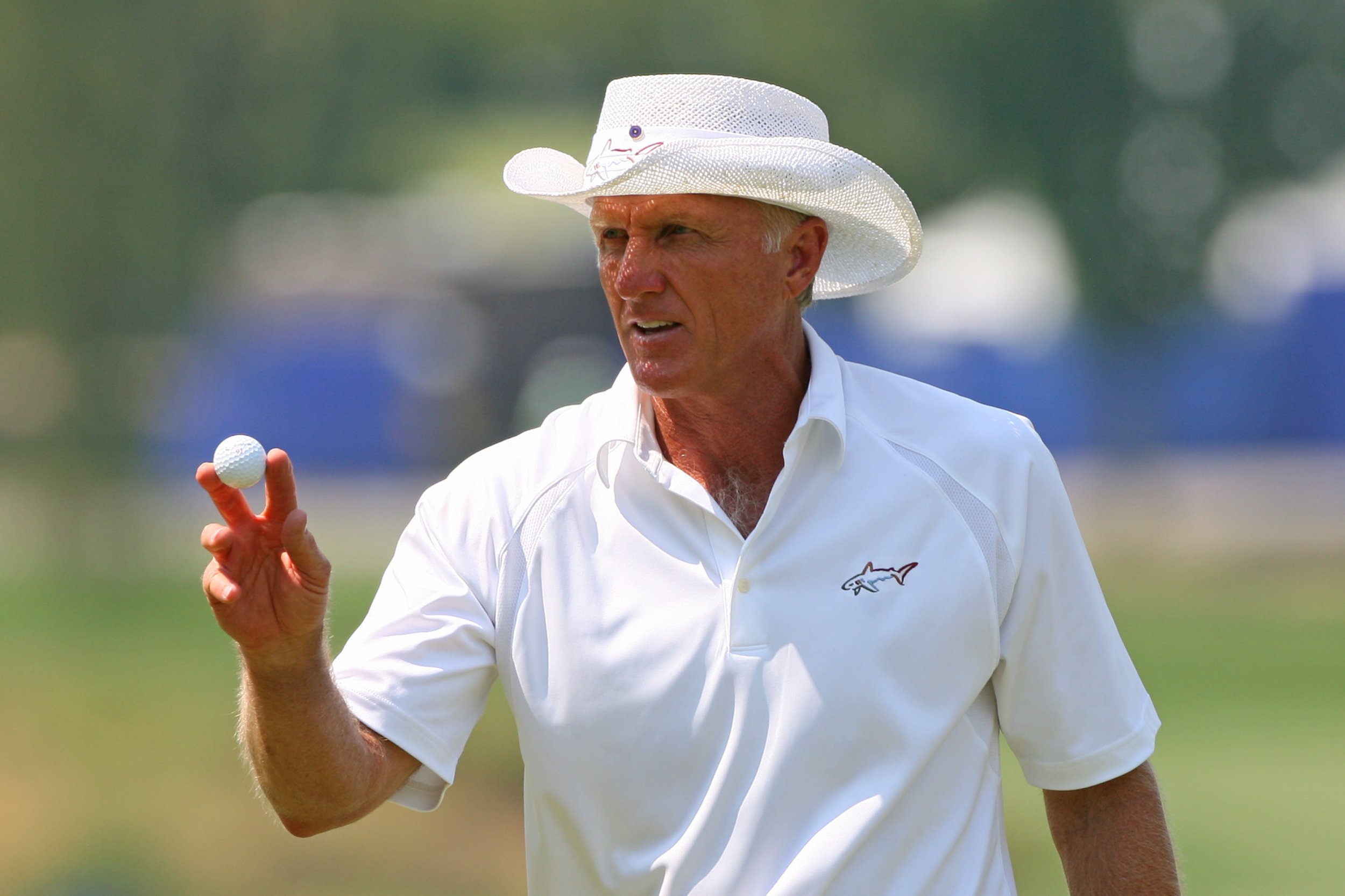 Greg Norman wearing a white polo shirt and white cowboy hat while holding a golf ball
