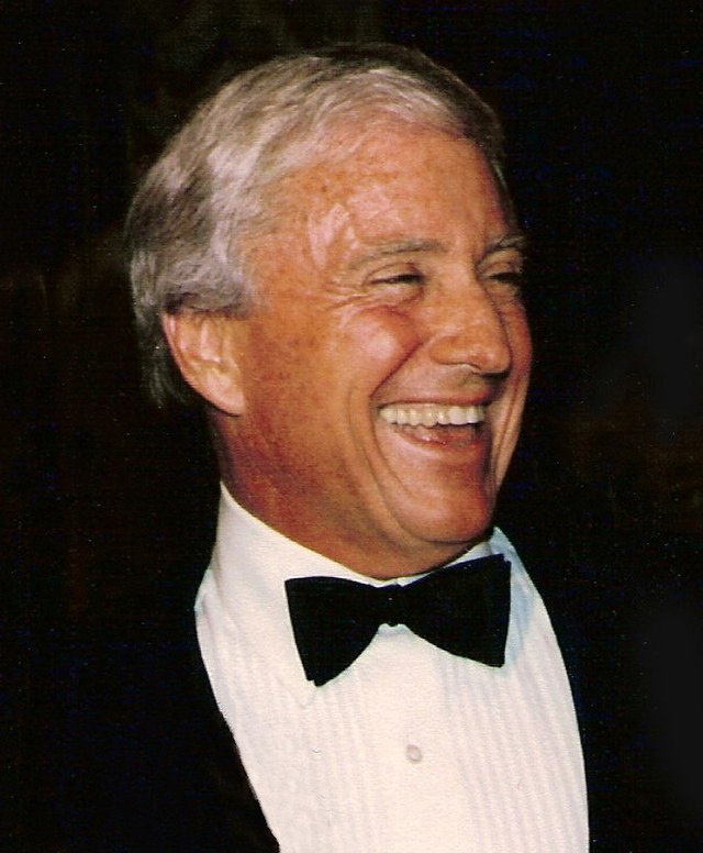 Smiling Merv Griffin wearing a black coat and black bow tie