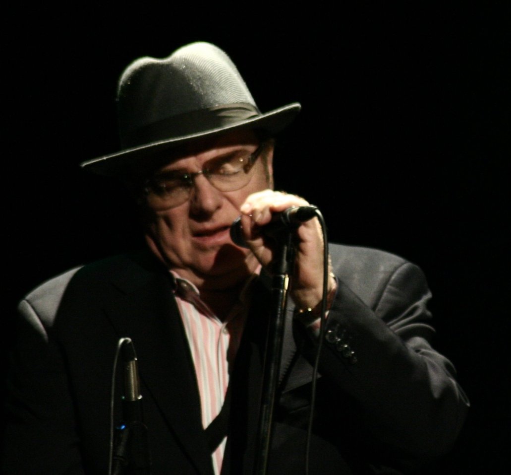 Van Morrison weaing a black suit and hat while holding a microphone