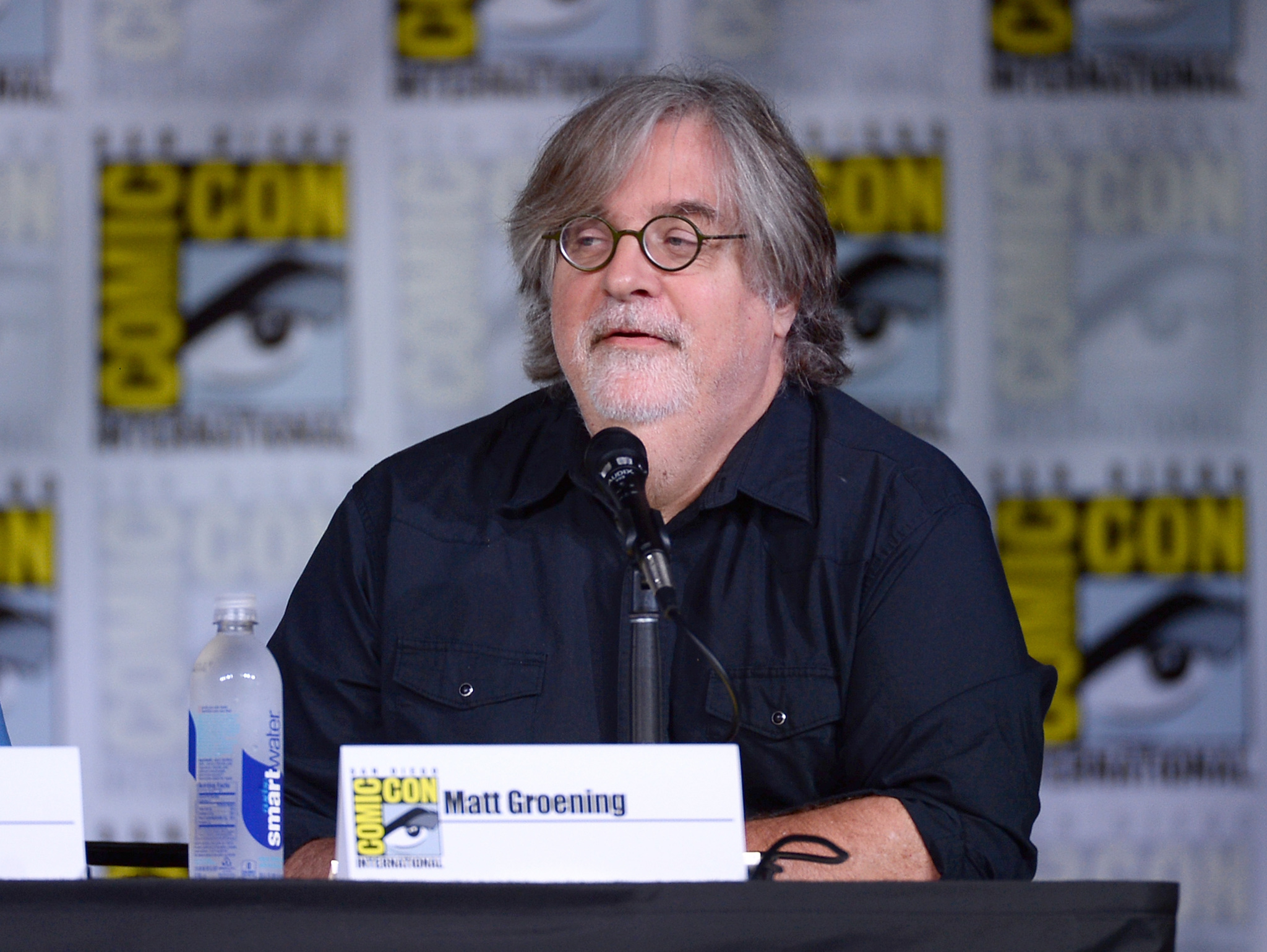 Maatt Groening wearing a black polo with mic in front of him at Comic con