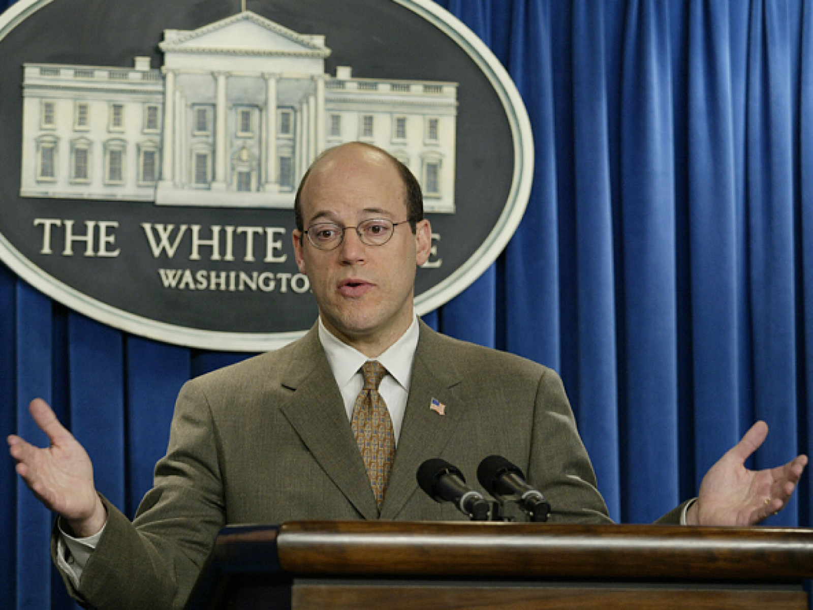 Young Ari Fleischer wearing a suit as he speaking into two microphones at the White House