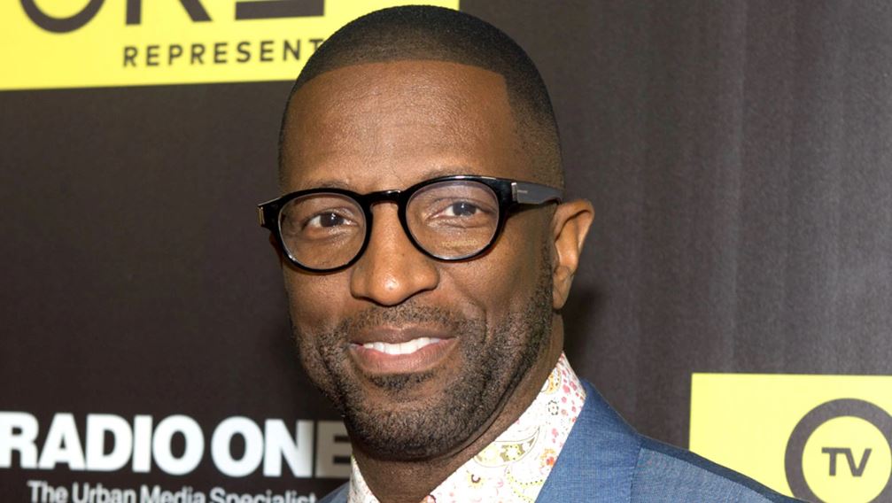 Rickey Smiley wearing a blue suit and a black eye glass at an event