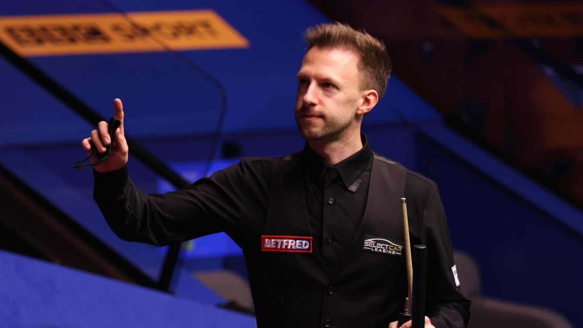 Judd Trump Posing In With One Hand In Air And Holding Snooker Stick In Other Hand