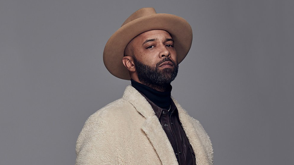 Joe Budden wearing a white fur clothe and a hat