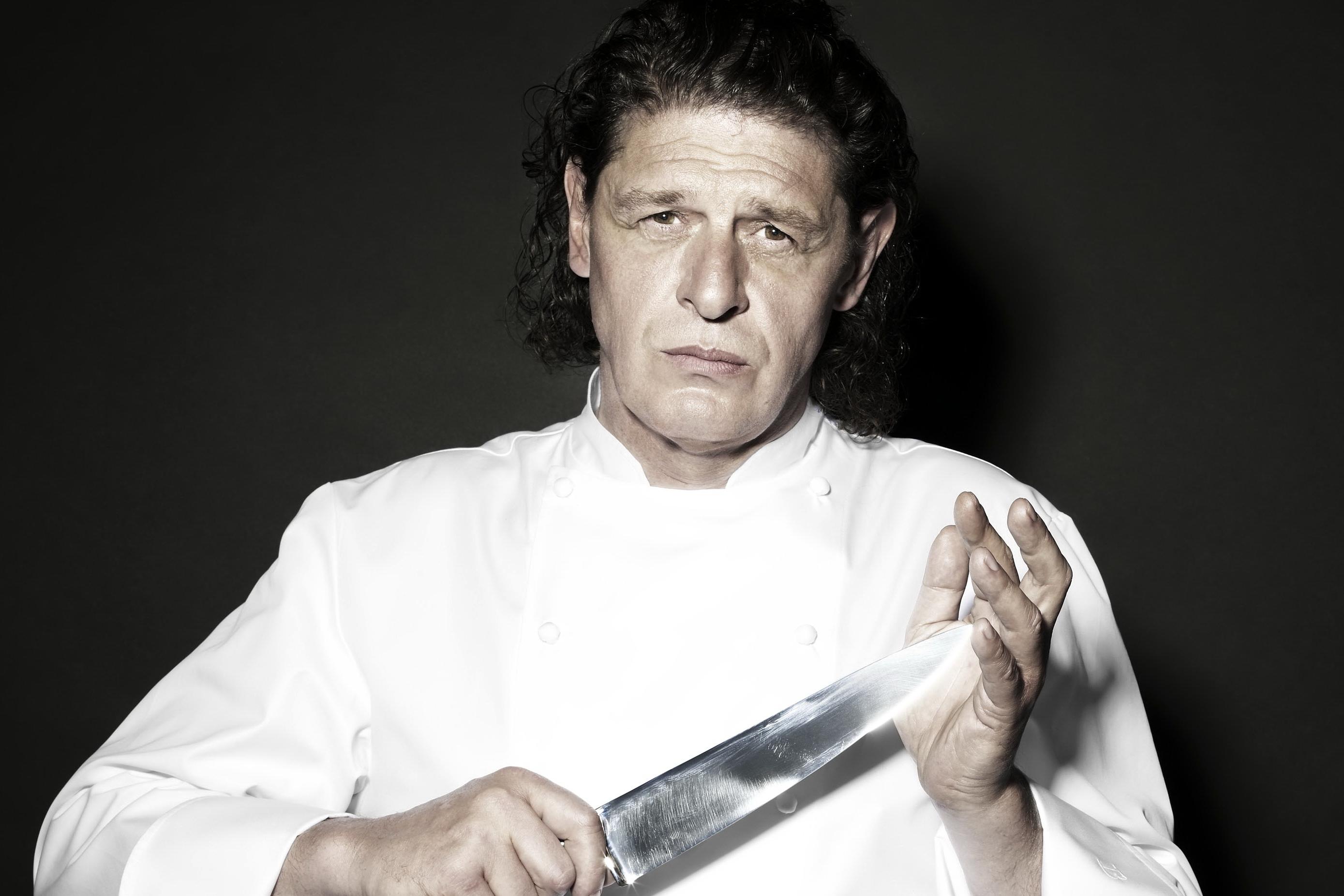 Marco Pierre White wearing a white chef uniform while holding a knife