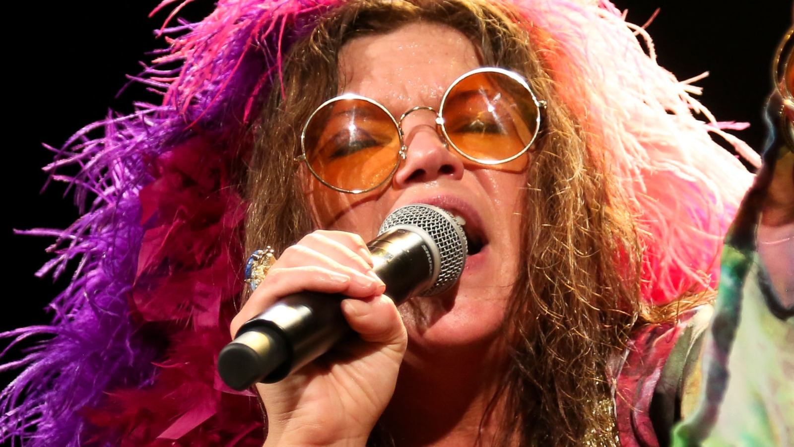 Janis Joplin wearing a round eyeglasses while holding a mic