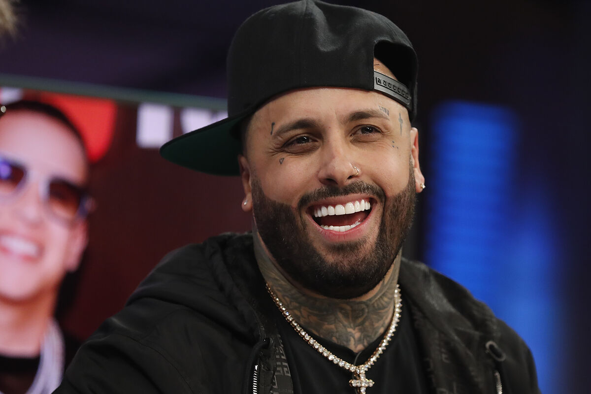 Nicky Jam wearing a black jacket, necklace, and black cap