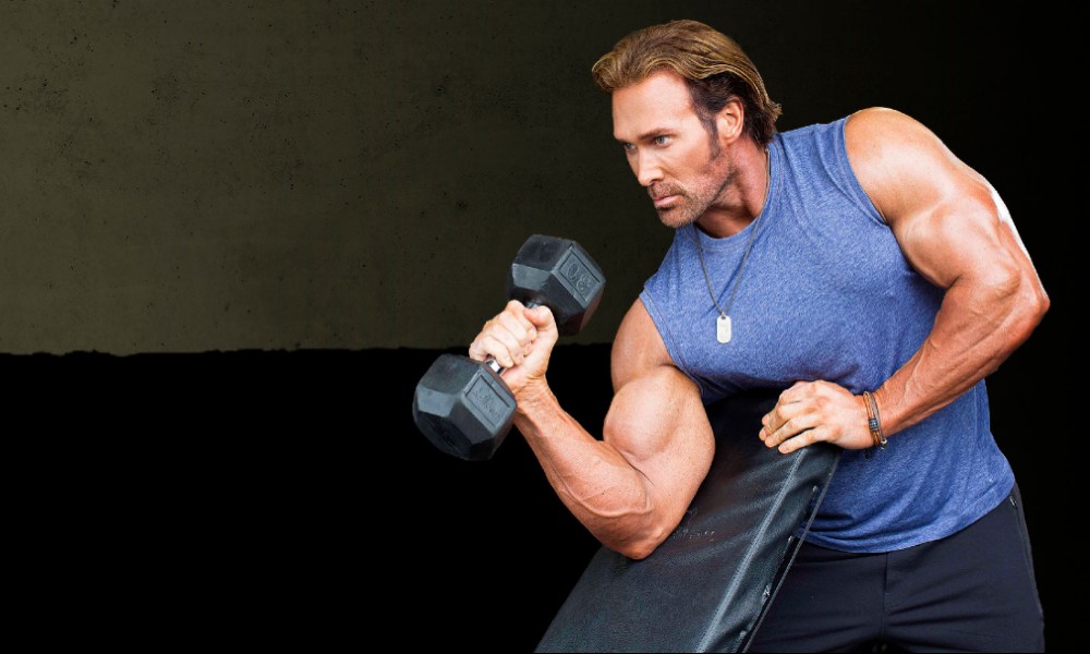 Mike O'Hearn wearing blue top while holding a dumbbell