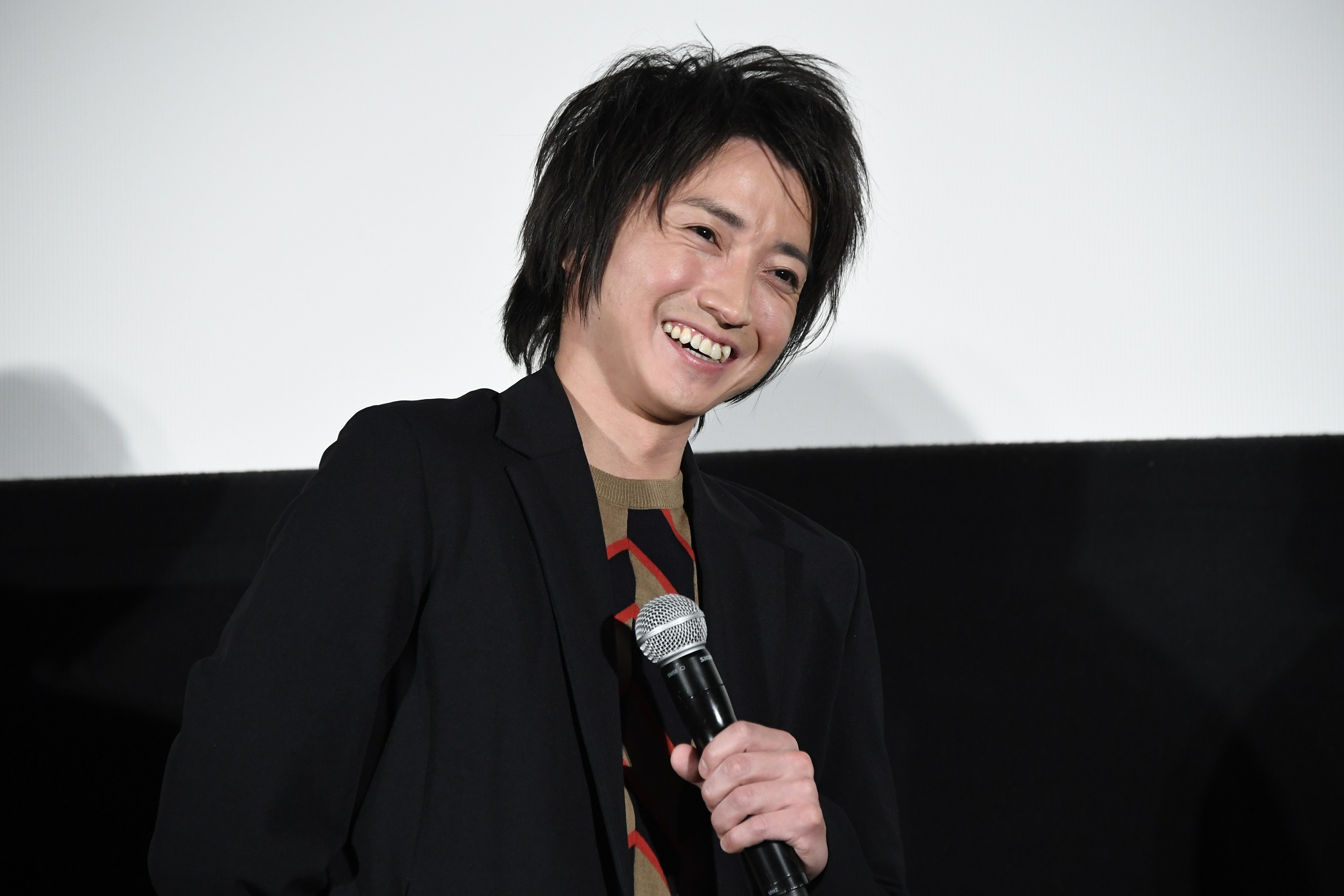 Tatsuya Fujiwara wearing a black coat while holding a mic