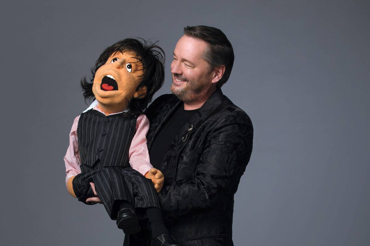 Terry Fator wearing a black suit with a puppet wearing a black stripes vest and slacks