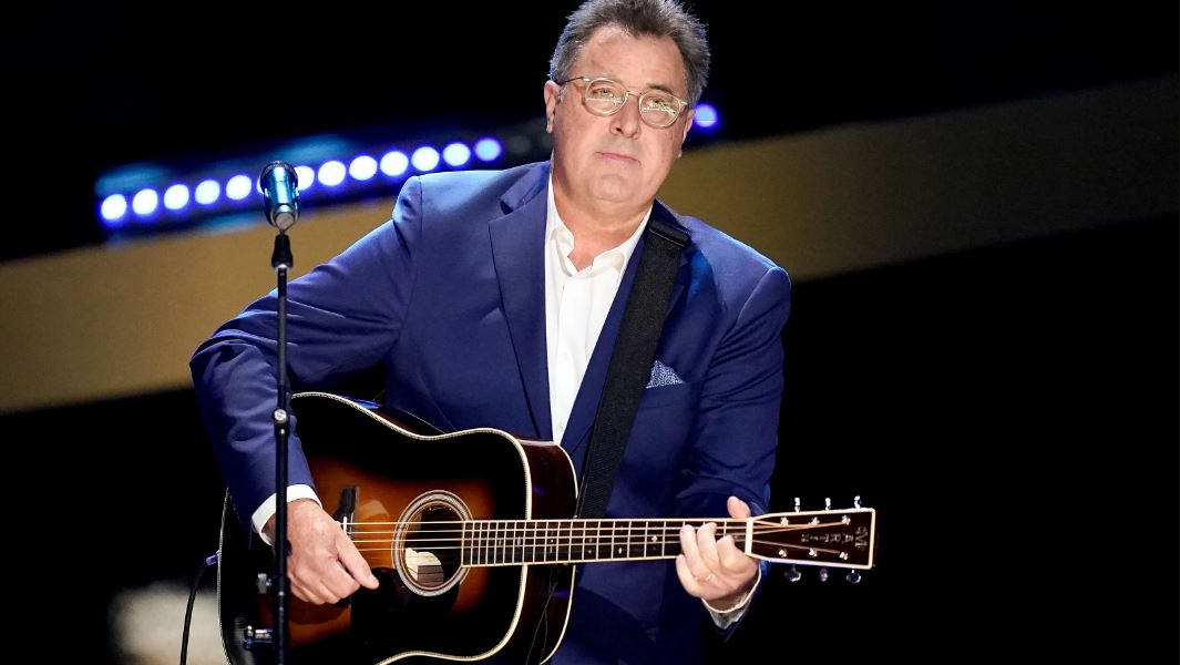 Vince Gill wearing a blue suit while playing a guitar during a performance