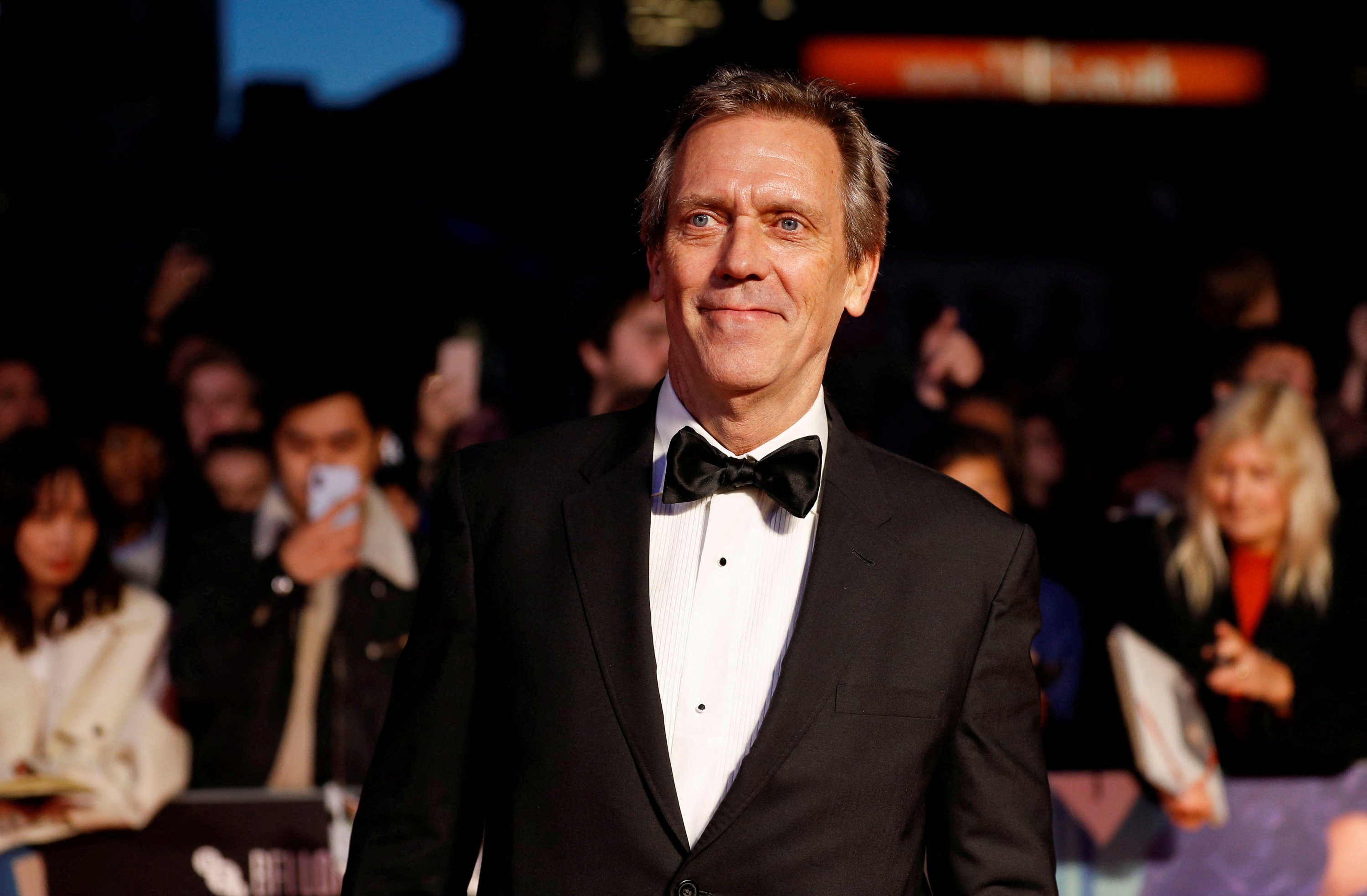 Hugh Laurie wearing a black suit and black bow tie