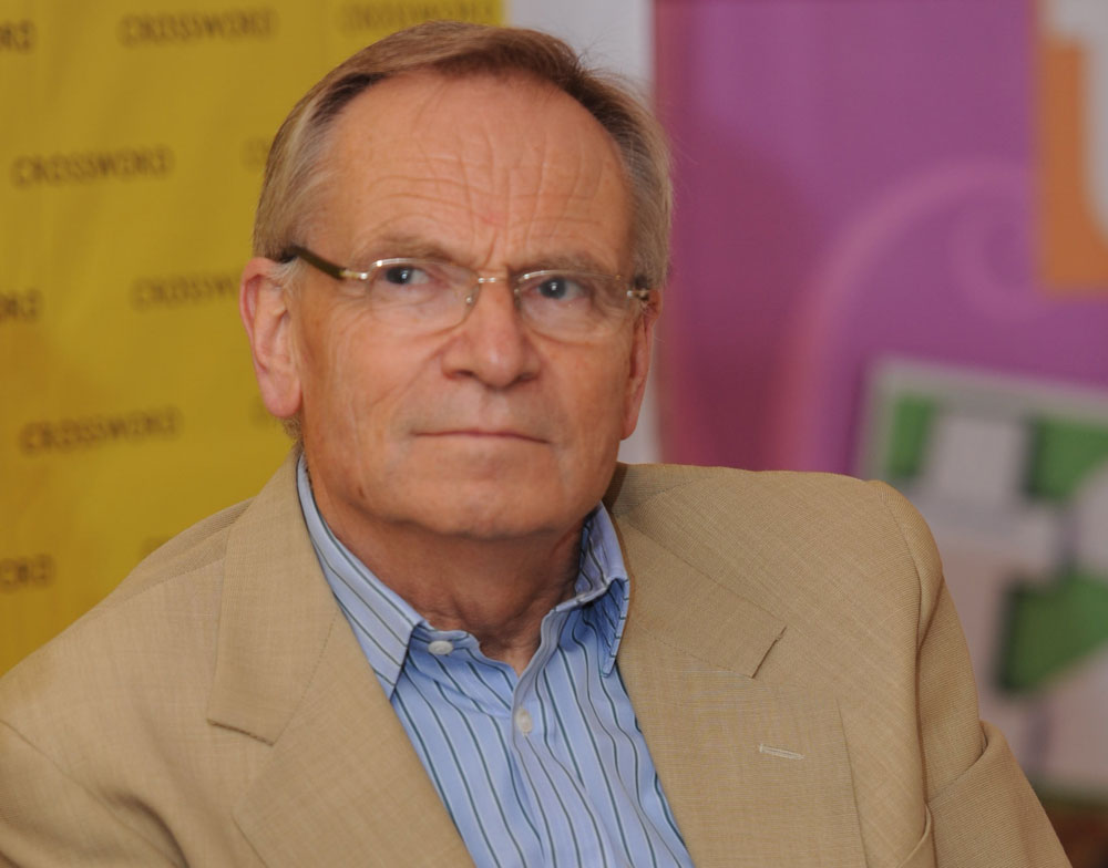 Jeffrey Archer wearing glasses, a brown coat with a blue striped undercoat