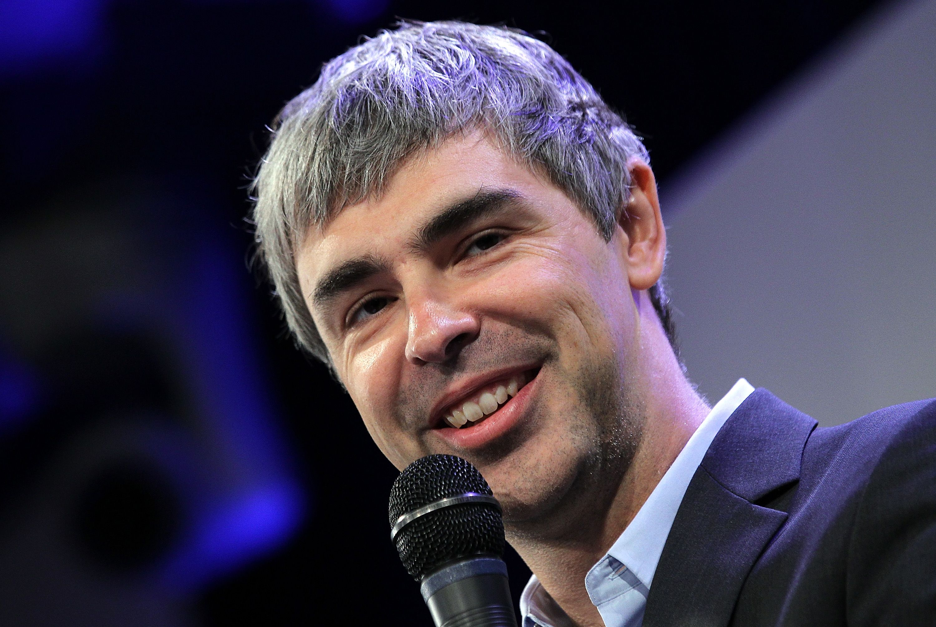 Larry Page wearing a black suit while holding a mic