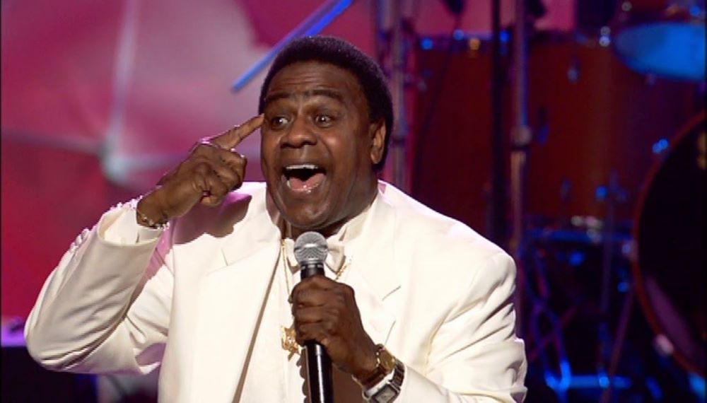 Al Green wearing a white suit while holding a mic