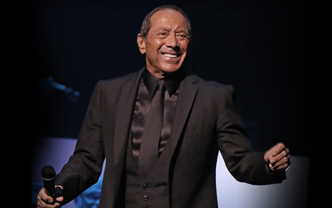 Paul Anka wearing a black suit while holding a mic