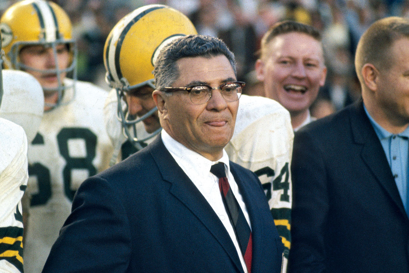 Vince Lombardi wearing a blue suit and eyeglasses