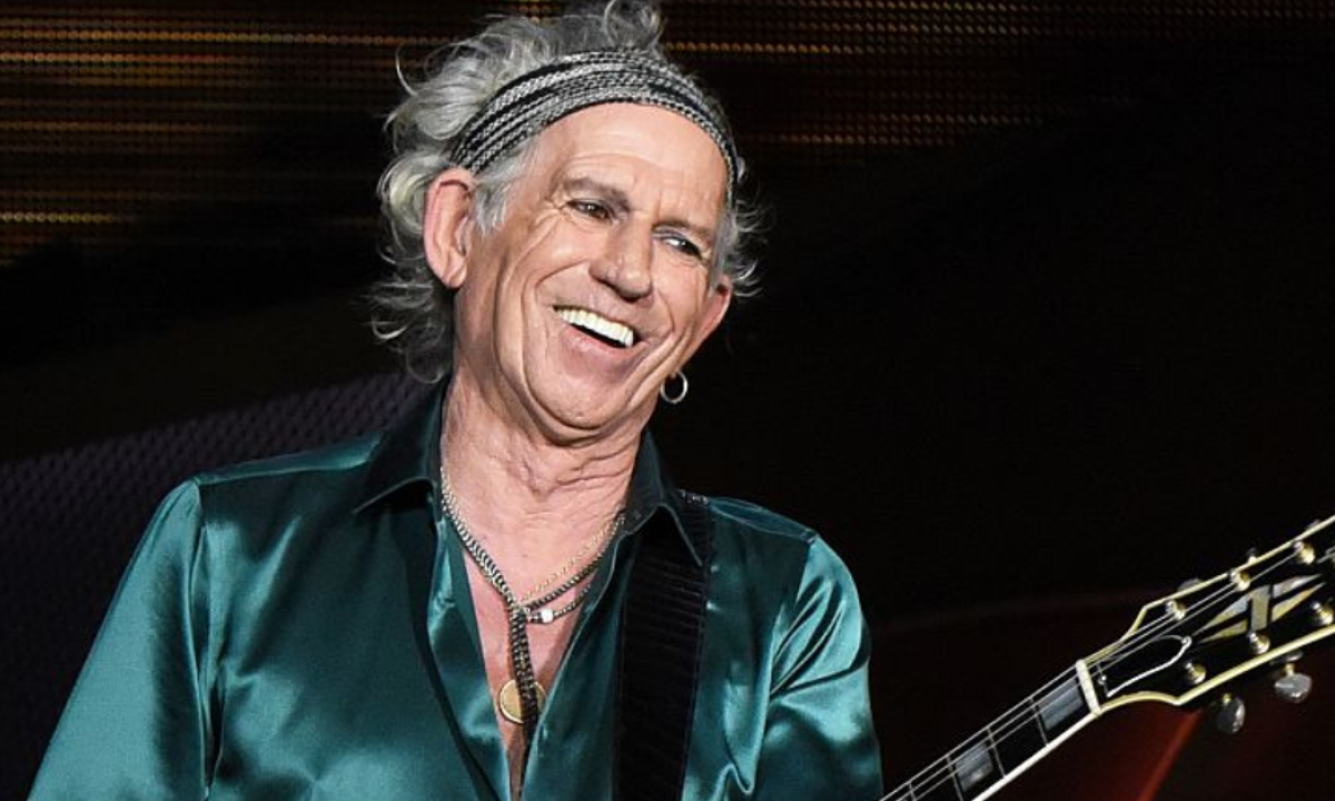Keith Richards wearing a green satin polo while holding a black guitar