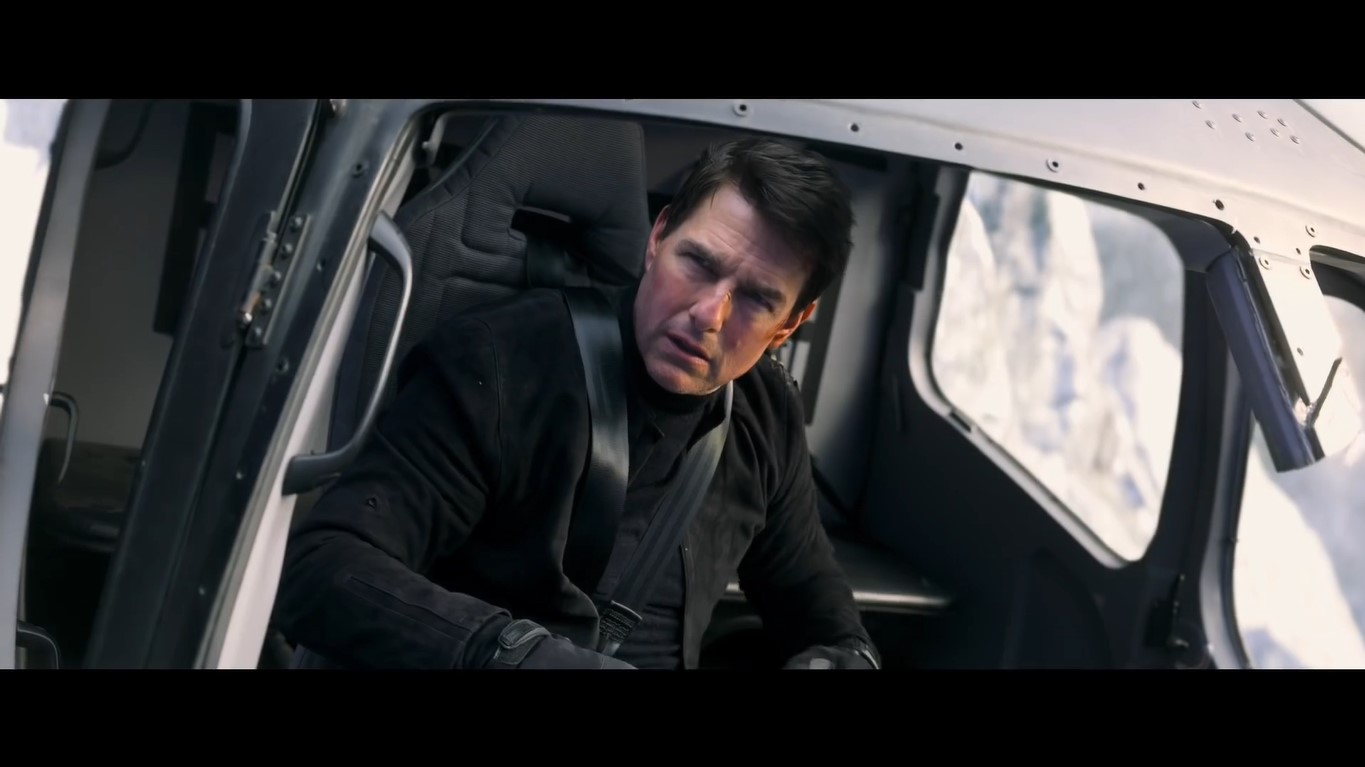 Tom Cruise in a helicopter wearing a black shirt, black long sleeve jacket and black gloves
