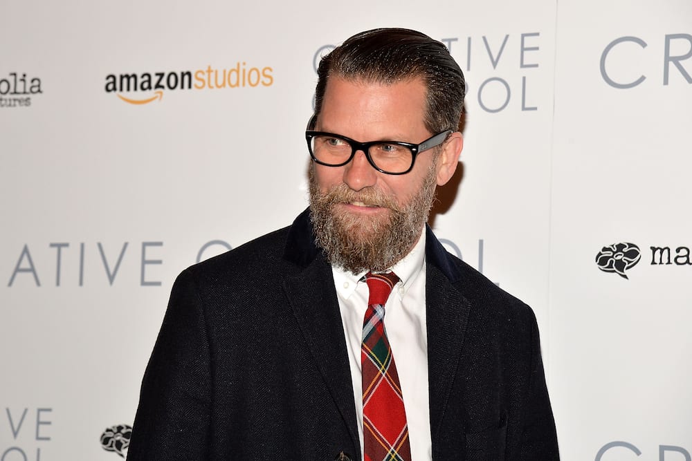 Gavin McInnes wearing a black suit and red neck tie
