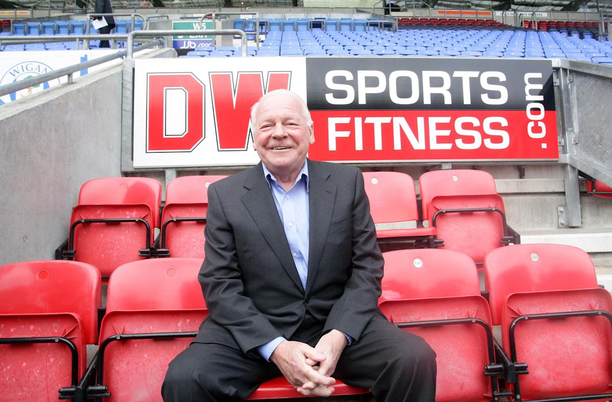 Dave Whelan wearing a black suit while sitting on red bleachers