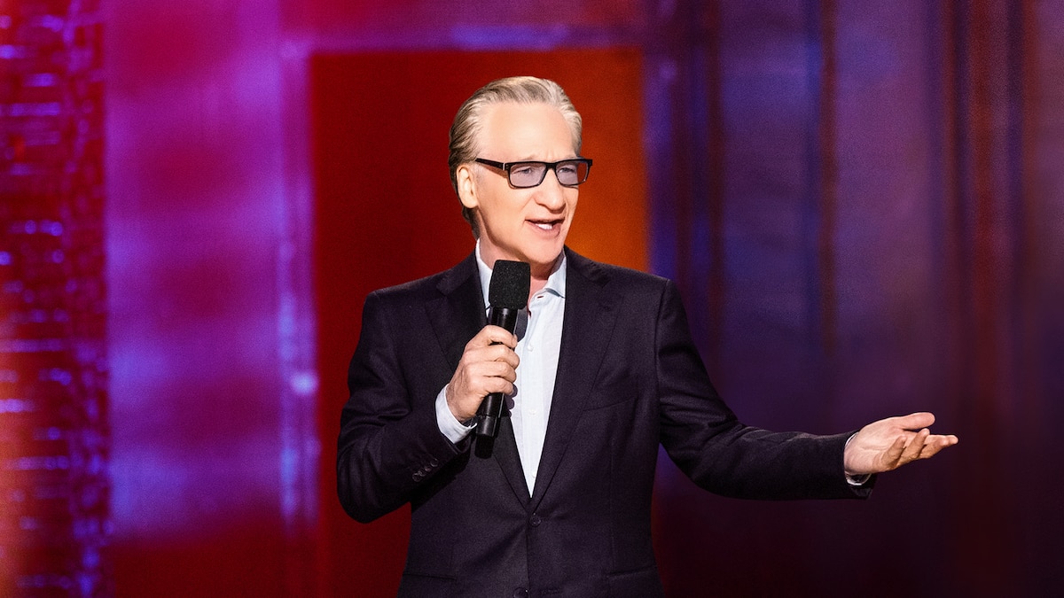 Bill Maher wearing a black suit while holding a mic