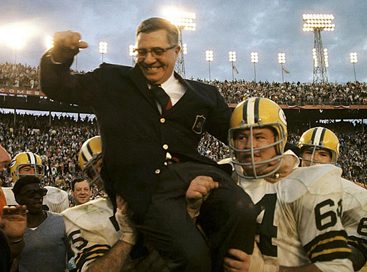 Footbaall players lifting Vince Lombardi while wearing a black suit