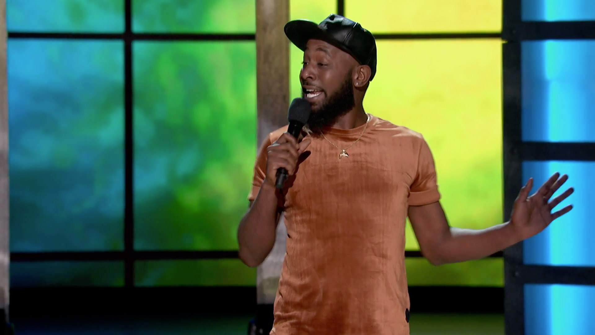 Karlous Miller wearing a velvet brown shirt and black cap while holding a mic