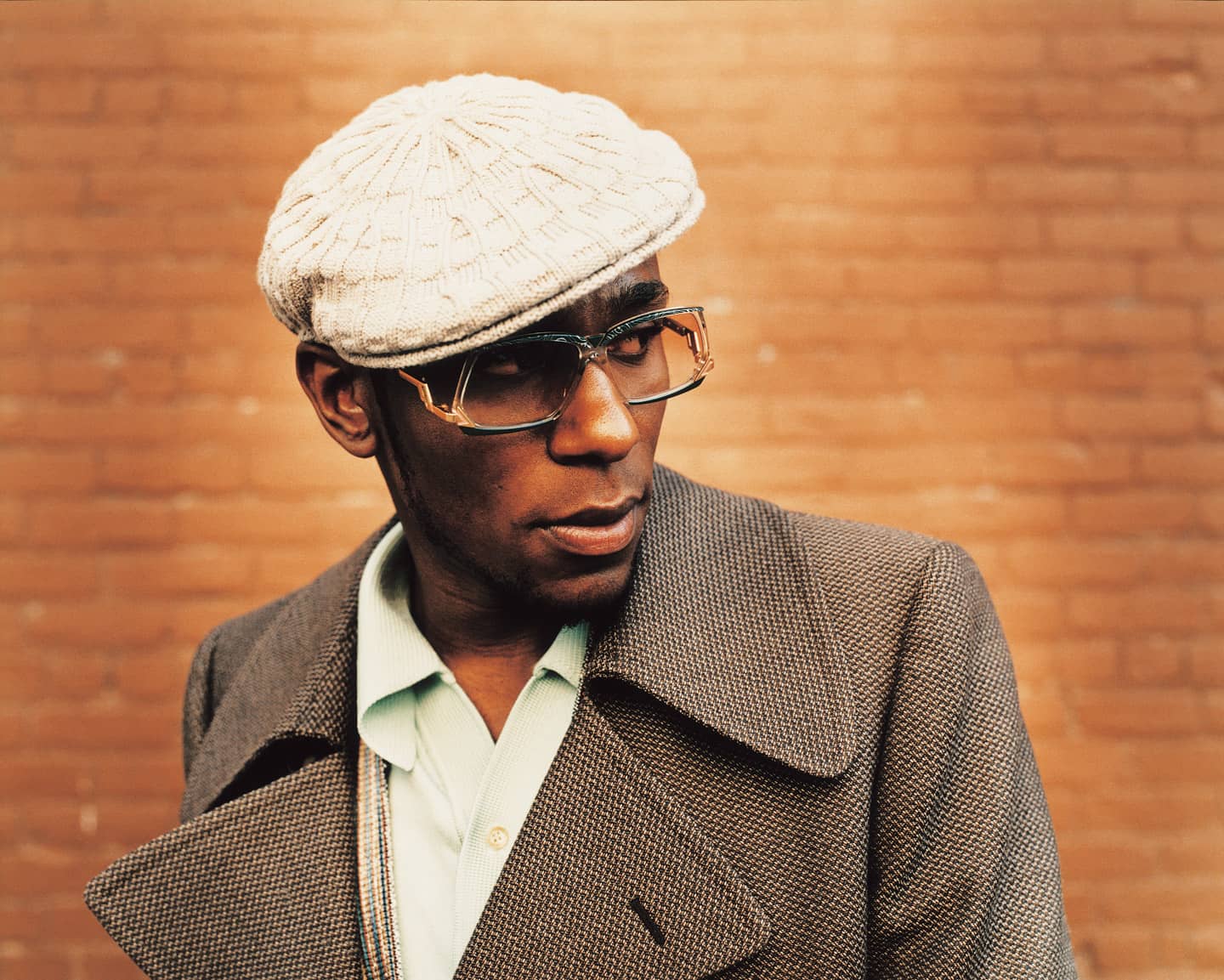 Mos Def wearing a brown coat and a hat