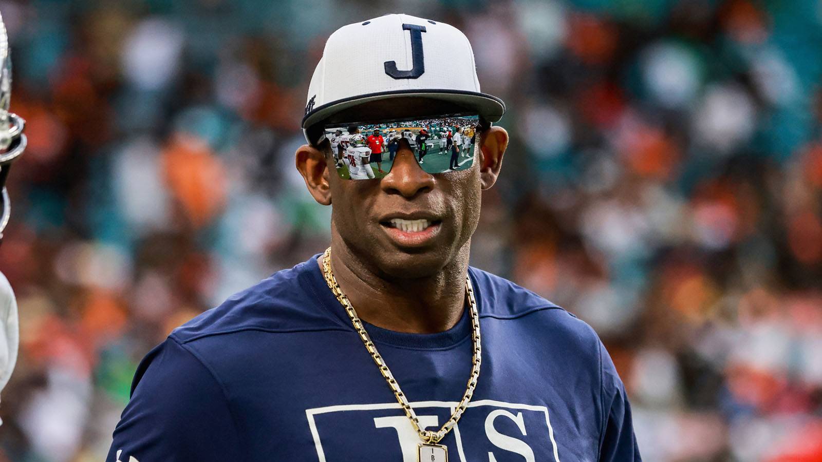 Deion Sanders wearing a blue shirt and white cap