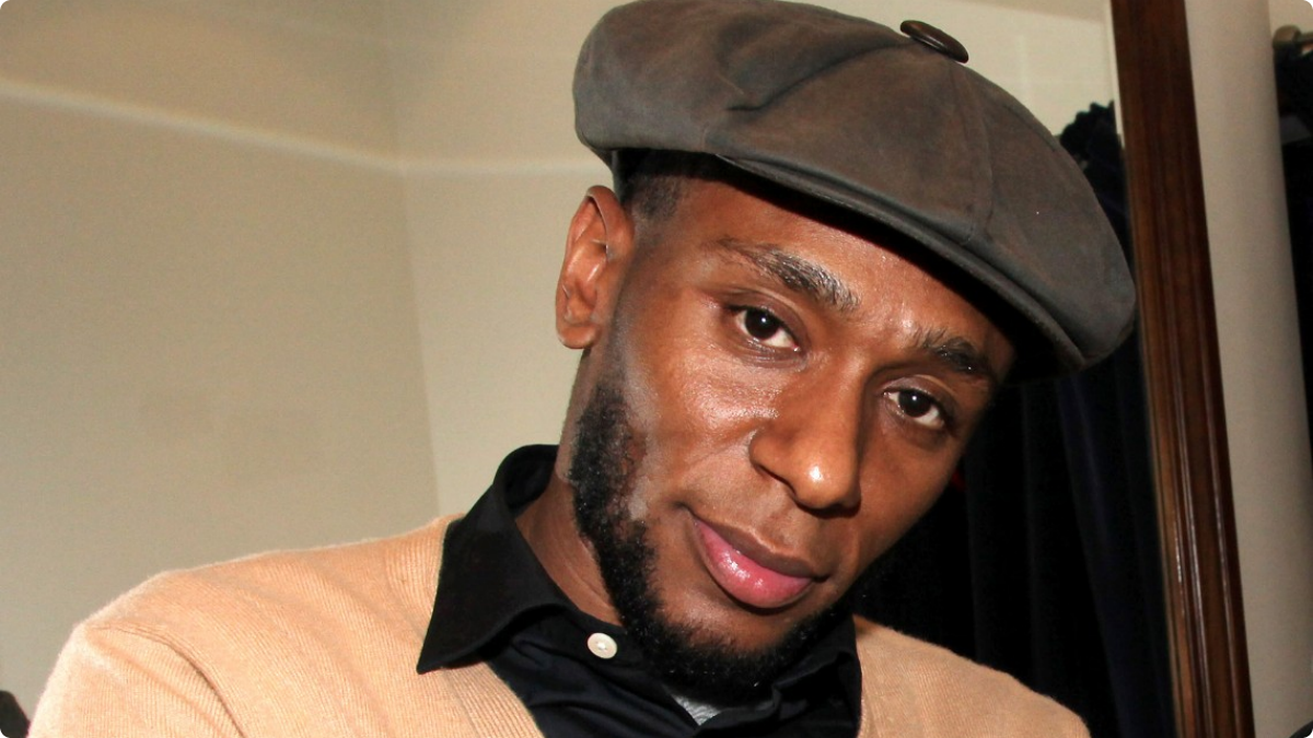 Mos Def wearing brown cardigan and a hat