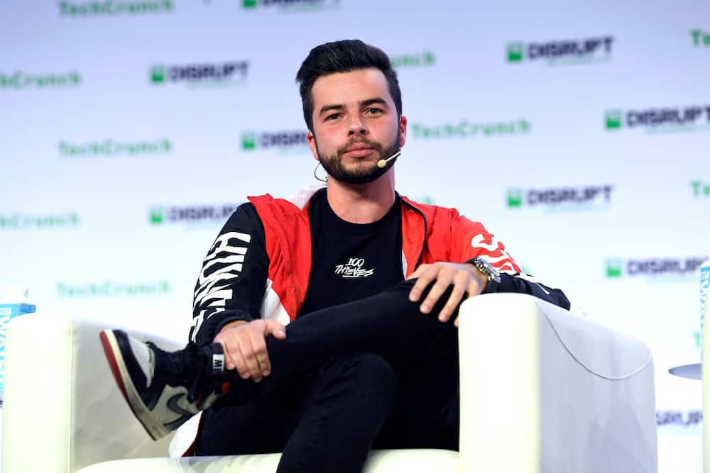 Nadeshot wearing a red and black jacket while sitting on a white couch