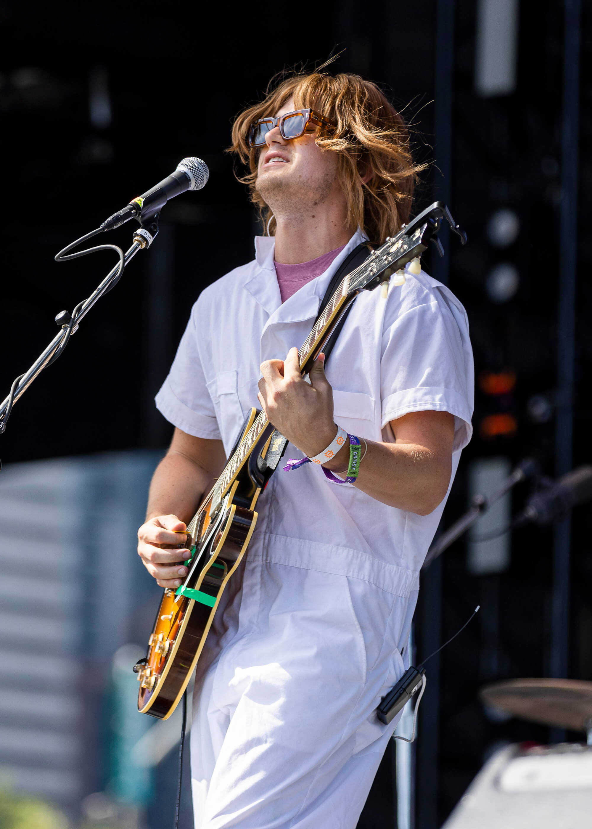 Joe Keery wearing all white and holding a guitar performing on stage