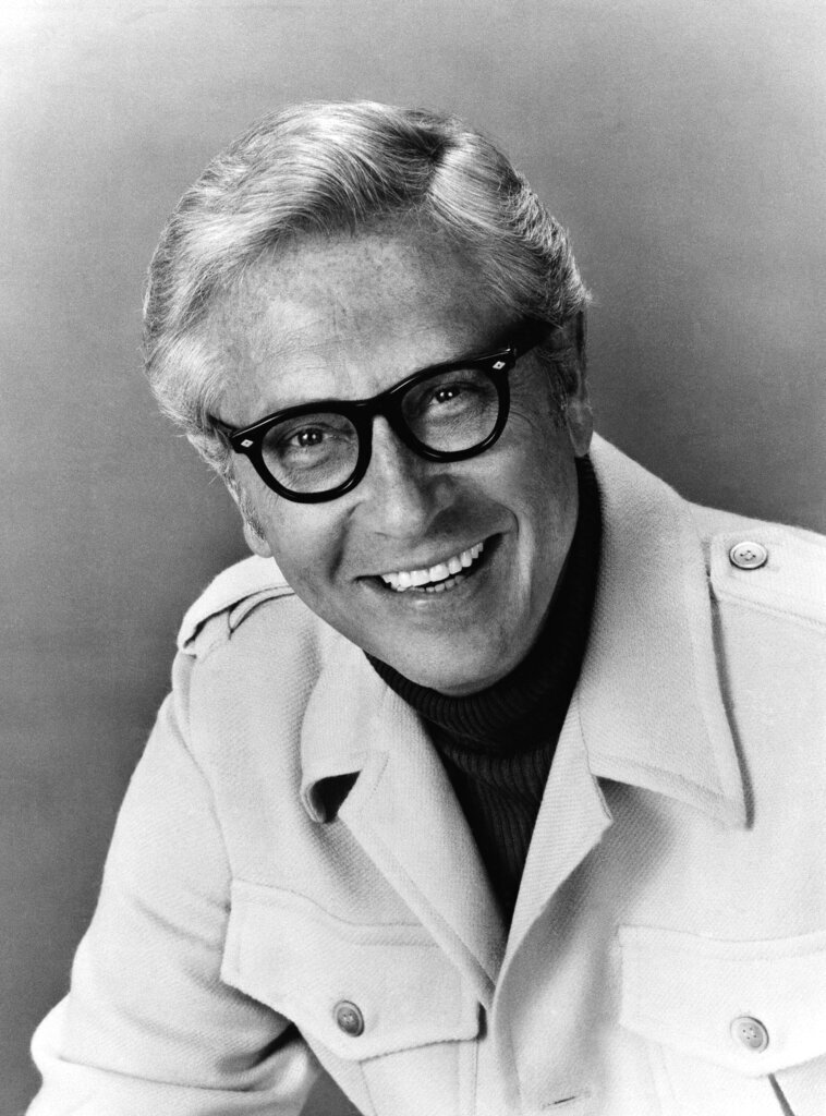 Allen Ludden wearing a trenchcoat and eyeglasses