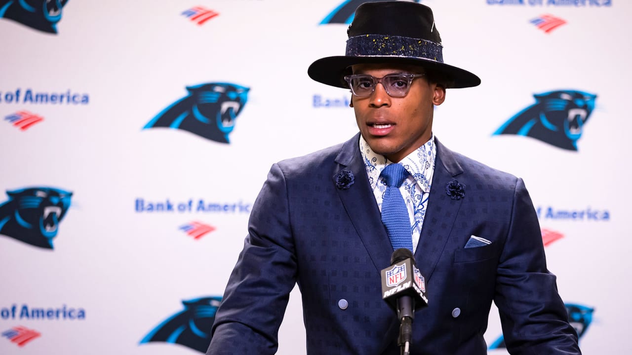 Cam Newton wearing a blue suit and black hat