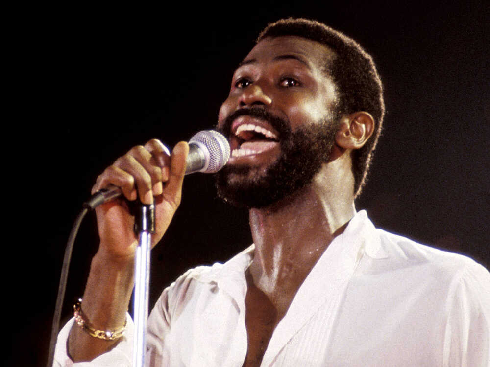 Teddy Pendergrass wearing white long sleeves while holding a mic and singing