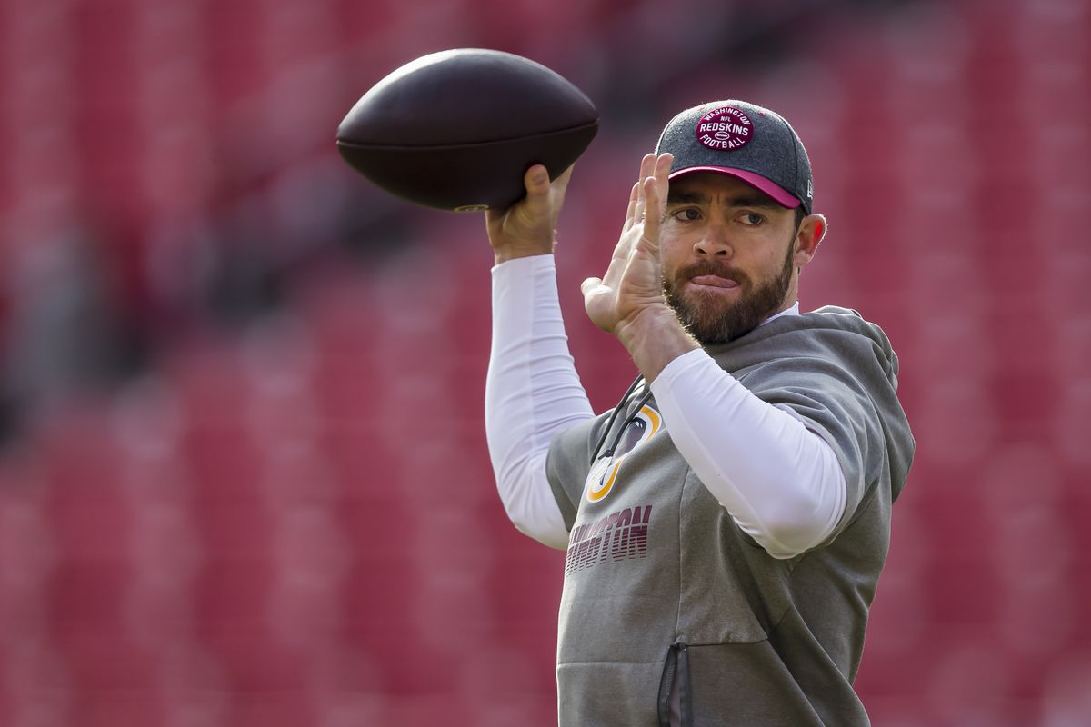 Colt McCoy weearng a gray hoodie and black cap while holding a football