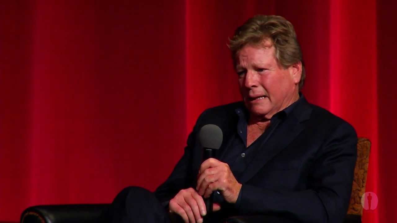 Ryan O'Neal wearing a black polo long sleeves while holding a mic