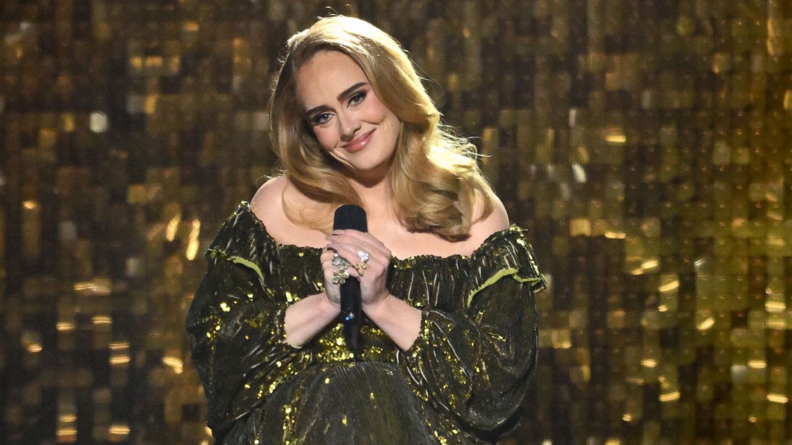 Adele wearing a gold dress while holding a mic