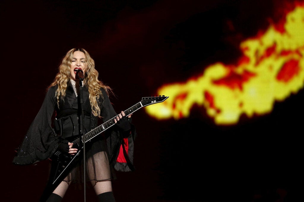 Madonna wearing a black outfit while holding an electric guitar