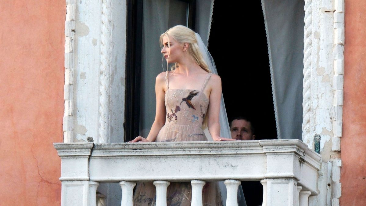 Anya Taylor-Joy wearing a beige dress and white veil on a balcony