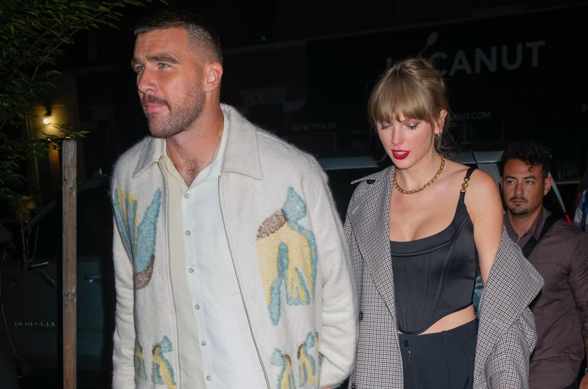 Travis Kelce wearing a white jacket and Taylor Swift wearing a black and white coat