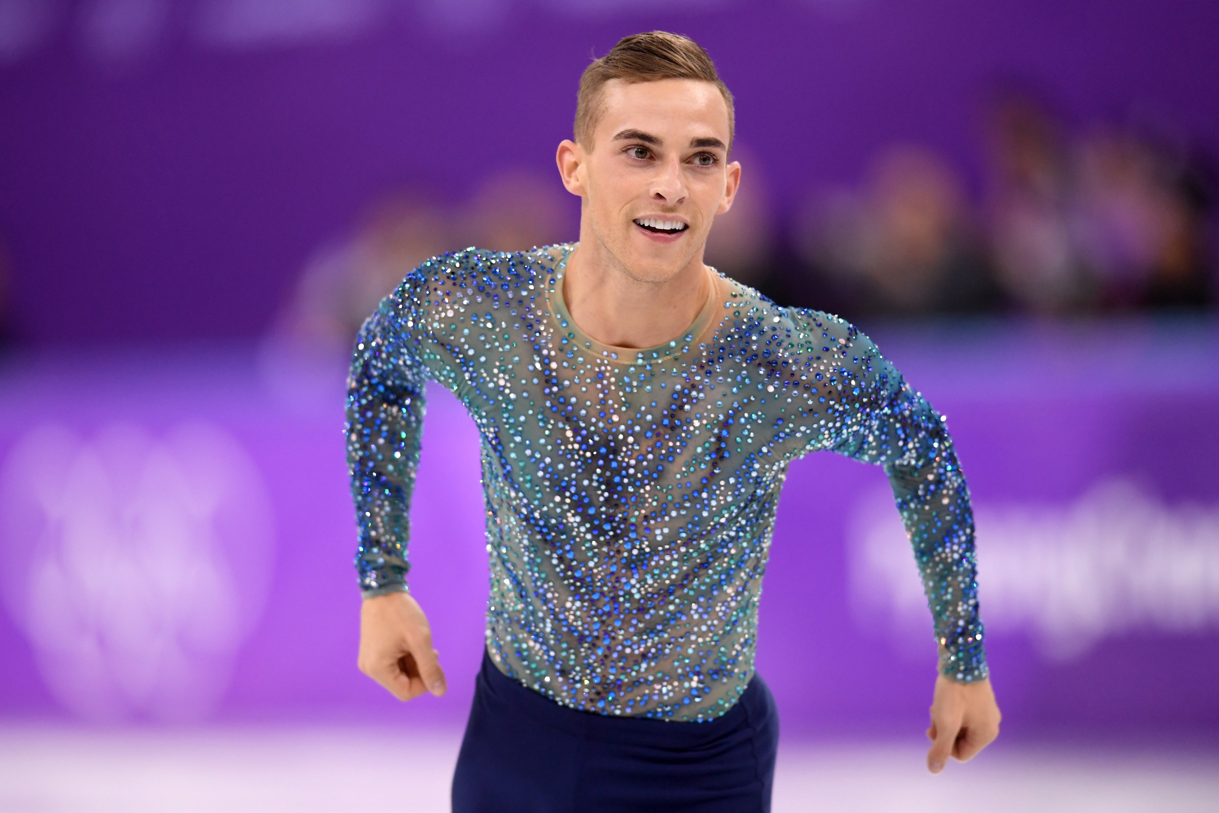 Adam Rippon wearing a sparkly blue top on an ice skating rink